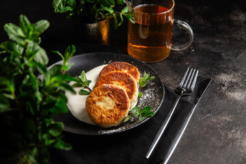 Cheesecakes with cream sauce and mint in a black plate on the table. Breakfast