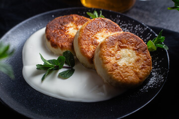 Cheesecakes with cream sauce and mint in a black plate on the table. Breakfast