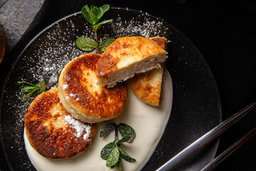 Cheesecakes with cream sauce and mint in a black plate on the table. Breakfast
