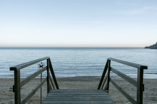 Wooden walkway leading to the beach in Costa Brava, Catalonia, Spain, captured under soft morning light, ideal for coastal retreats and tourism visuals.