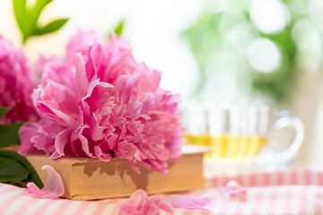 Pink peonies resting on vintage book on striped tablecloth with cuo of tea.