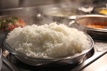 A large plate of fluffy white rice steaming in a cafeteria, ready to be served to hungry patrons.