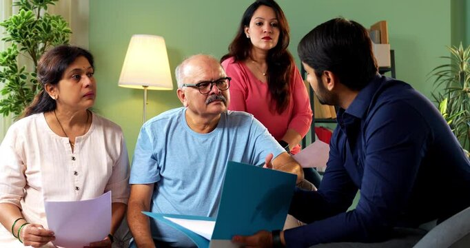 Senior Indian couple with young daughter discussing financial paperwork with male advisor or bank agent in formal wear at home — concept of real estate, loan, insurance or savings consultation