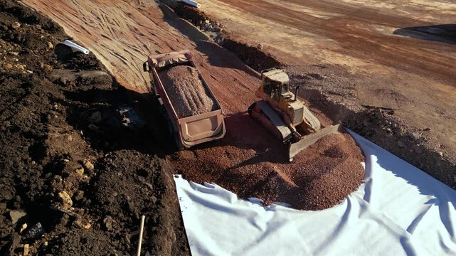 High angle top down late afternoon footage of bulldozer maching covering layers of geotextile with dirt and soil for the construction of a highway. Freeway build site with geosynthetic fabric burried
