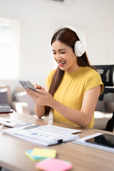 Business woman with laptop using mobile phone and listening music through headphones at home office.
