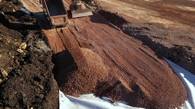 High angle top down late afternoon footage of bulldozer maching covering layers of geotextile with dirt and soil for the construction of a highway. Freeway build site with geosynthetic fabric burried
