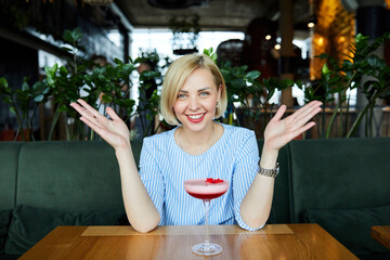 Portrait of attractive young woman drinking coctail in cafe indoor. Beautiful blonde woman relaxing at the bar and drinking a cocktail