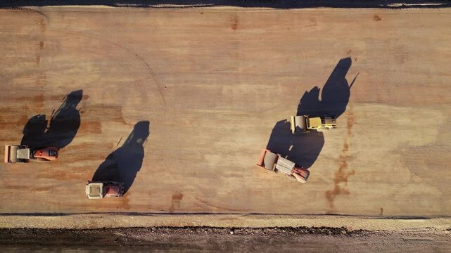 Top-down aerial image of heavy vibratory compactors working in parallel on an expansive new road construction project, highlighting teamwork, precision ground leveling, scale of civil engineering