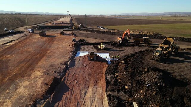 High angle top down late afternoon footage of bulldozer machine covering layers of geotextile with dirt and soil for the construction of a highway. Freeway build site with geosynthetic fabric burried

