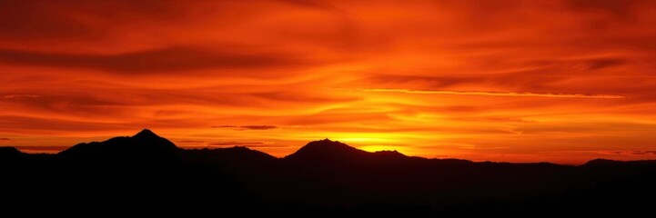 Fototapeta premium Fiery Sunset Silhouette: Mountains at Dusk in a Dramatic Landscape