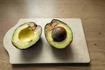 Halved avocado with pit on wooden cutting board.