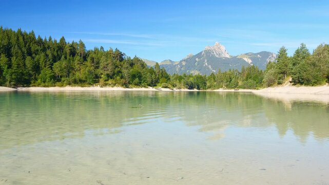 Turquoise alpine lake surrounded by lush hills and forest in Reutte Tirol, peaceful shoreline and mountain reflections at Urisee
