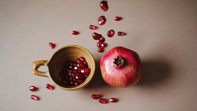 A still life composition featuring a bowl of pomegranate seeds next to a cup filled with pomegranate juice