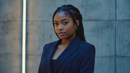 A woman stands in front of a wall, wearing a blue suit