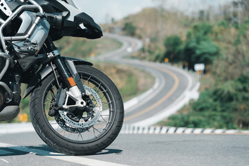 Obraz premium A motorcycle is parked on a winding road with green trees and hills in the background, suggesting adventure and travel.