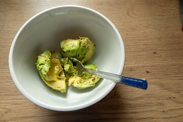 Avocado flesh on spoon in white bowl.