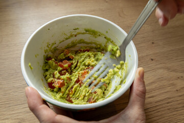 Mixing avocado and diced tomatoes for homemade guacamole.