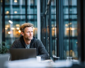 Man Contemplating at Window Table with Laptop and Glass of Water