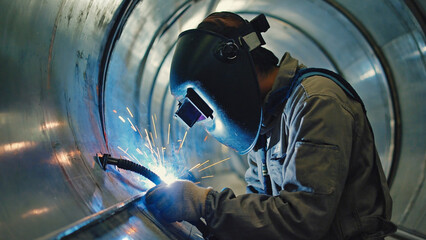 A person wearing a welding mask and gloves welding a piece of metal, with sparks flying everywhere