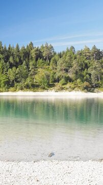 Still mountain waters of Urisee with turquoise hues and green forest banks in Reutte Tirol, relaxing alpine nature retreat