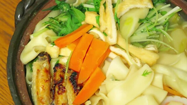 Nagoya's specialty, Kishimen noodle stew in miso broth, Japanese style noodles, deep-fried tofu, carrots, chicken, and Naruto