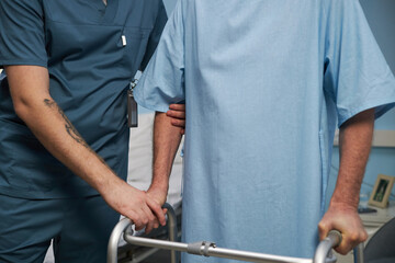 Healthcare professional supporting elderly patient with walking frame in medical facility. Focus on care and assistance for elderly patient