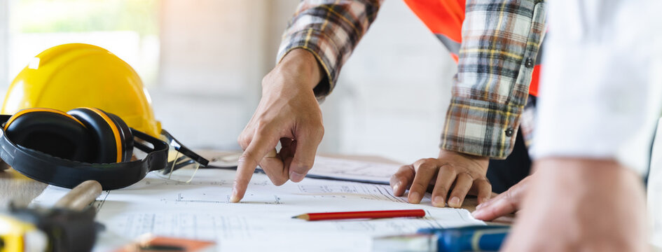Close up hands of businessman from consultancy service discussing with project contractor and reviewing blueprint for build real estate facilities.