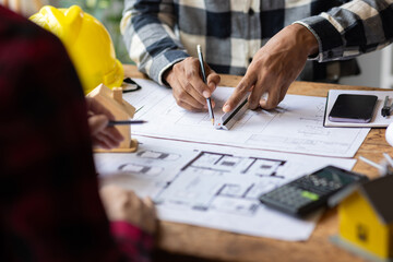 Architect using ruler and pencil reviewing blueprint of architectural project. Two architects are...