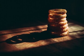 A vertical stack of golden, crispy fried onion rings in dramatic light on a wooden surface.