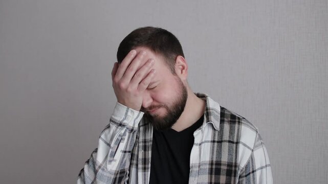 Bearded displeased young man man showing facepalm gesture against neutral studio background