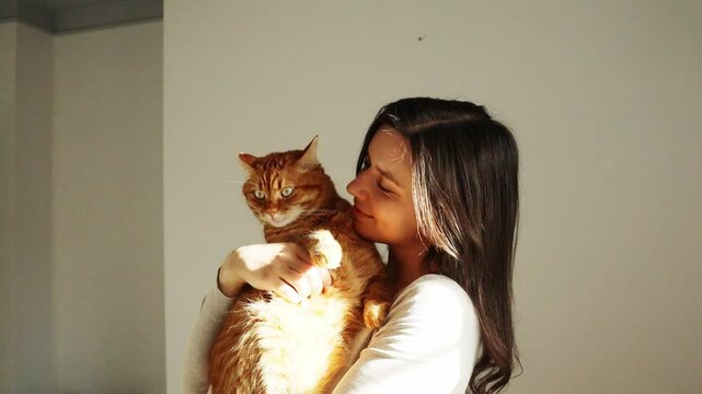 Girl brunette dancing with an orange cat and petting him in the sunlight at home
