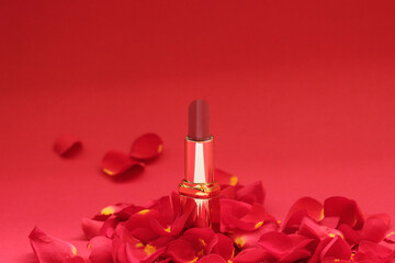 Luxury red lipstick surrounded by rose petals on red background. Glamorous beauty concept for cosmetics, makeup products, and feminine elegance.