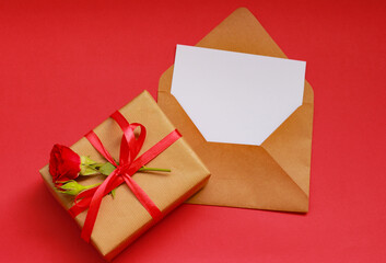 Gift box wrapped in kraft paper with red rose and ribbon, next to an envelope and card on red background — a beautiful setup for expressing love on Mother’s Day.