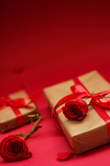 Elegant gift box wrapped in kraft paper with a red satin ribbon and decorated with a red rose on a vibrant red background. Romantic composition with soft focus, perfect for love-themed celebrations.
