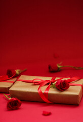 Beautiful gift box wrapped in kraft paper with a red satin ribbon and adorned with a single red rose, placed on a bright red background. Perfect for celebrating Mother's Day. 