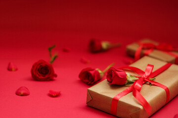 Beautiful gift box wrapped in kraft paper with a red satin ribbon and adorned with a single red rose, placed on a bright red background. Perfect for celebrating Mother's Day. 
