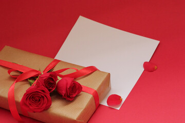 Romantic Valentine's Day scene with a gift wrapped in kraft paper and red ribbon, surrounded by red roses and petals, with blank space for a love message or greeting card.