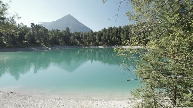 Tranquil turquoise lake in Tyrol with calm reflections and forested slopes, peaceful mountain escape at Urisee near Reutte