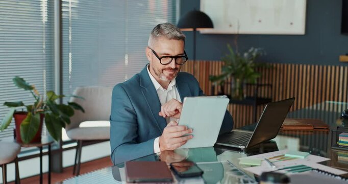 Tablet, laptop and businessman in office for research, trading and financial results online. Technology, reading and happy mature manager check stock price for investment, economy analysis and profit
