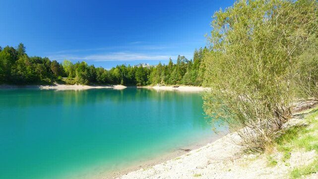 Alpine lake Urisee with turquoise waters, green hills, and quiet beach area in Reutte Tirol, perfect for summer holiday getaways