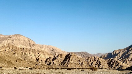 Golden sediment mountain range reveals rippling wave-like erosion, showcasing nature sculpted art formed by tectonic activity, wind forces, and millennia of geological exposure.