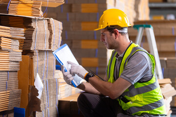 man paper warehouse worker take note on clipboard checking inspecting quality cardboard corrugated carton in storage. Large industry in paper product line manufacturing.