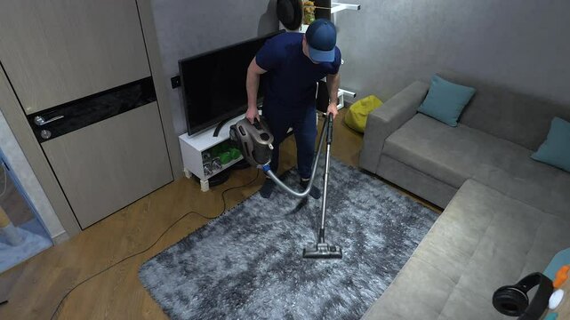 Top view. Professional cleaner vacuums a shaggy rug in an apartment with a brush with fast speeds, cleaning fabric furniture, cleaning an apartment with a vacuum cleaner. Slow motion.