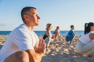 Group of people in yoga squat pose on beach at summer sunset - Yoga session at sunset, concept of...