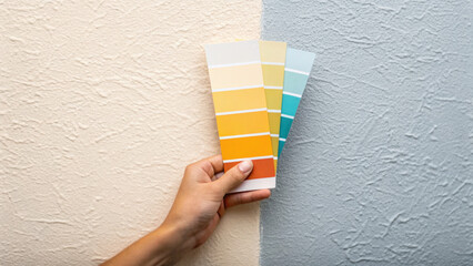 Hand holding color swatch with yellow and blue shades against textured wall, showing paint color options for home improvement and decoration ideas