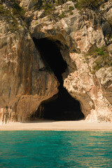 Turquoise water laps gently on the sandy beach of cala luna, with its iconic caves carved into the...