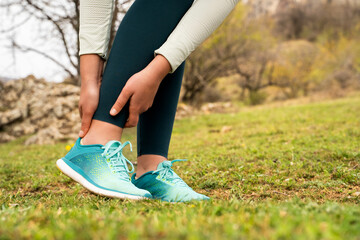 Woman holding ankle injury, feeling pain in her foot in nature park, sports trauma during trail run, massaging leg, suffering from strain spasm in calf outdoors, discomfort, feet ache, healthcare