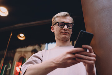 Urban stylish male with smartphone standing near modern architecture, casual outfit, relaxed and confident, enjoying digital connectivity, everyday technology concept, outdoor communication