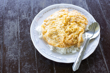 Steamed rice topped with omelet on a white plate on a wooden table