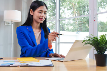 Asian businesswoman communicating with clients online using laptop in professional working environment. She is confident and articulate, demonstrating her skills in virtual communication.